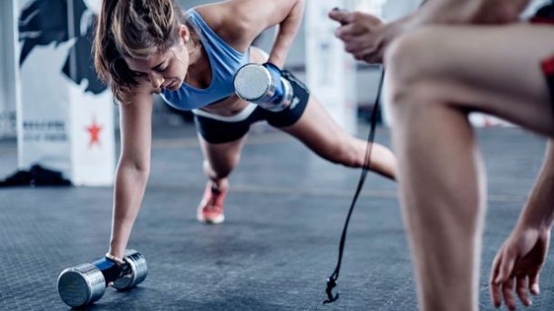 Fitness-trainer-keeping-time-with-woman-doing-dumbell-push-ups